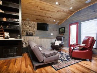 Rustic living room with wood-paneled ceiling, gray stone fireplace, leather couch, and red accent chairs